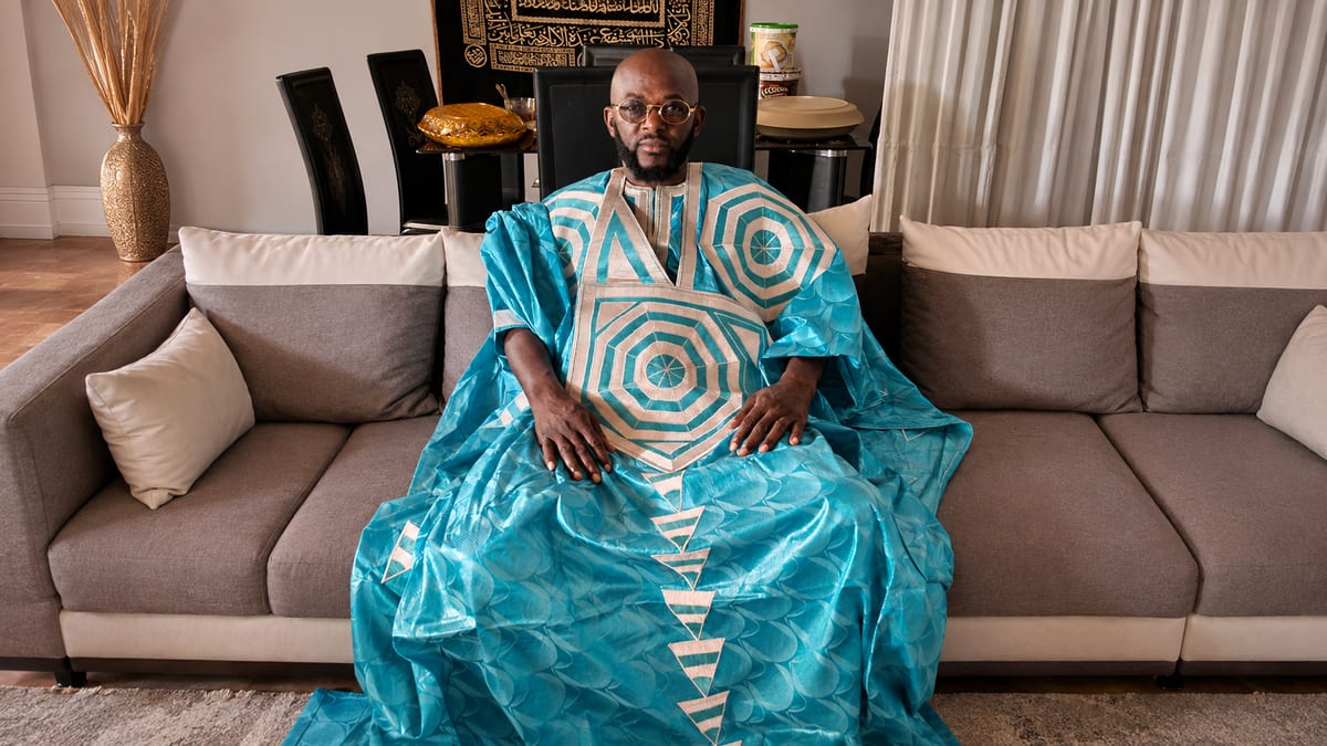 Marabout Djibril in a turquoise boubou, seated in his living room